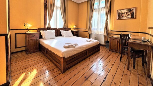 Een hotelkamer met een houten bed, twee nachtkastjes, een bureau en een stoel.
