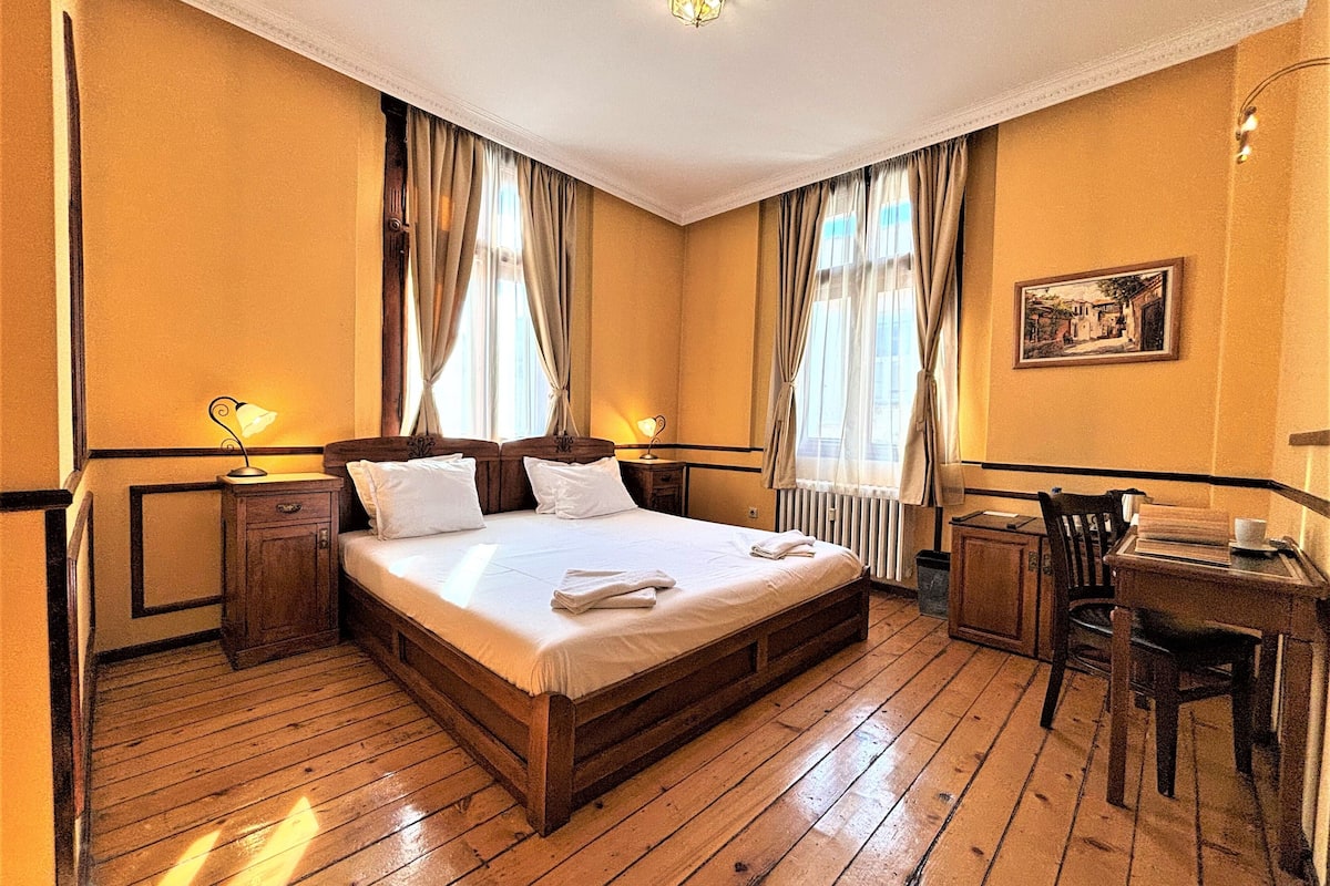 A hotel room with a wooden bed, two bedside tables, a desk, and a chair.