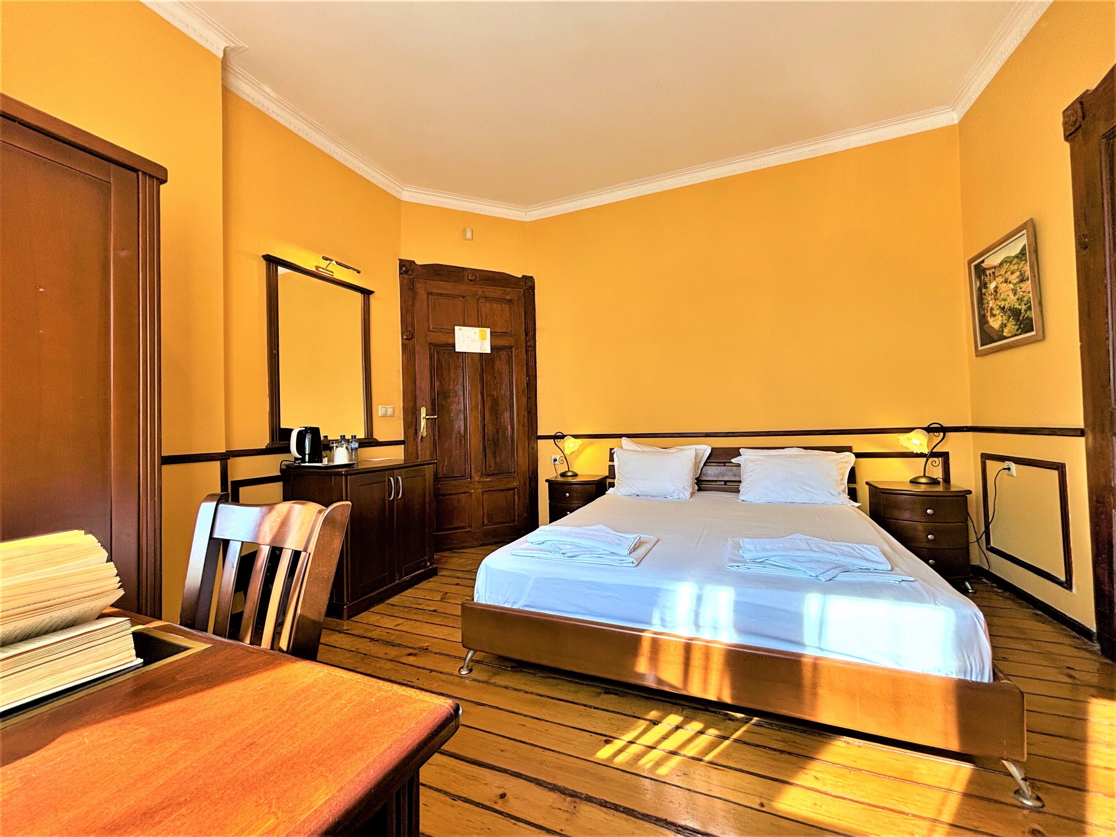 Een hotelkamer met een houten bed, een bureau met stoel, een dressoir en een spiegel.
