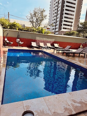 Piscina con sillas de descanso y una pared de ladrillo rojo.