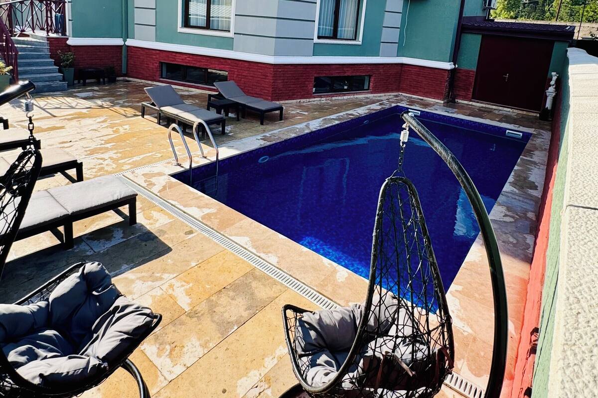 A two-story house with a swimming pool, outdoor seating, and air conditioning units.