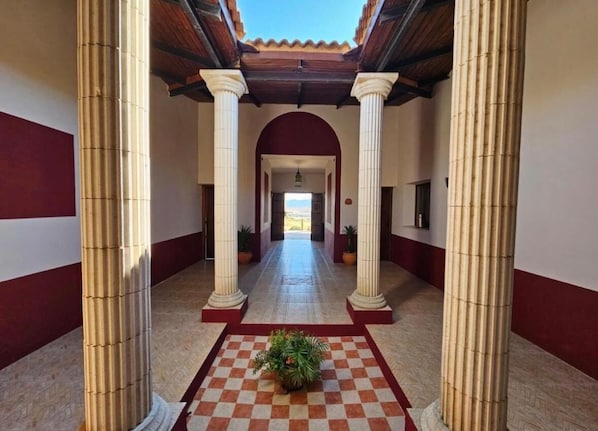 A corridor with columns, checkered flooring, and a potted plant. - Villa Aemilius (Don Alvaro)