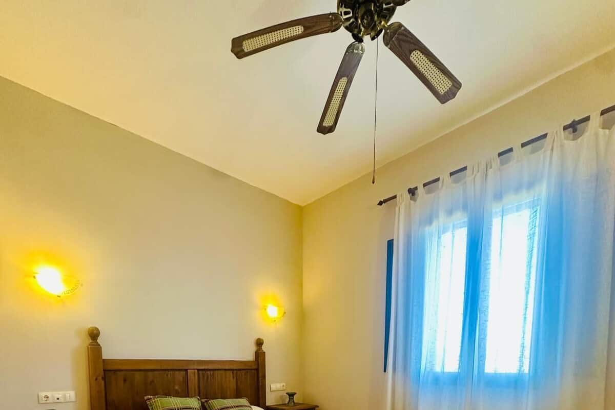 A bedroom with a wooden bed, two bedside tables, a ceiling fan, and a window with curtains.