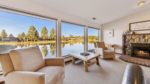 Un salon spacieux doté de grandes fenêtres, d’une cheminée et offrant une vue sur un lac et des arbres.