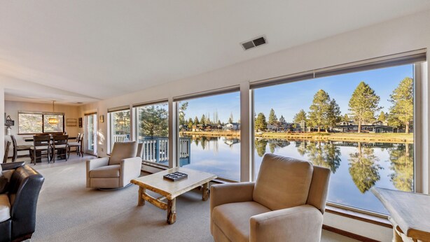 Un salon spacieux doté de grandes fenêtres donnant sur un lac, et aménagé avec un canapé, des fauteuils et une table basse.