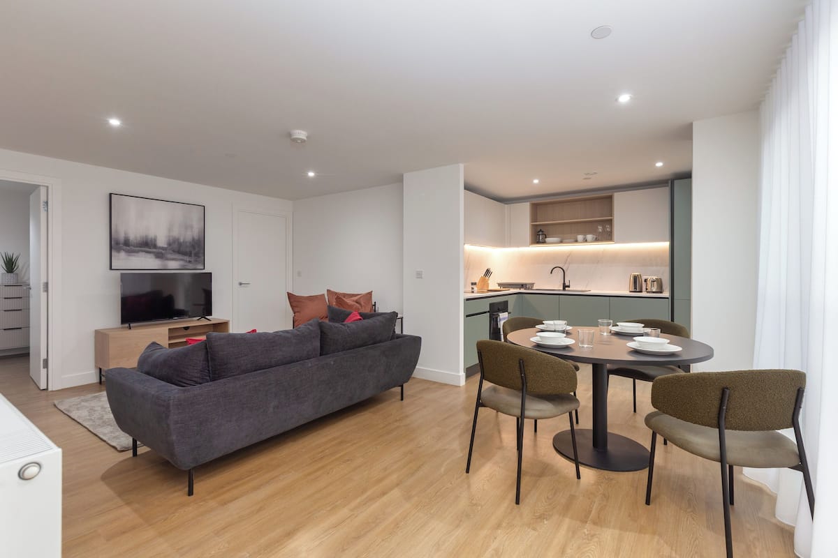 A modern living room with a grey sofa, a TV, and a dining area with a table and chairs.