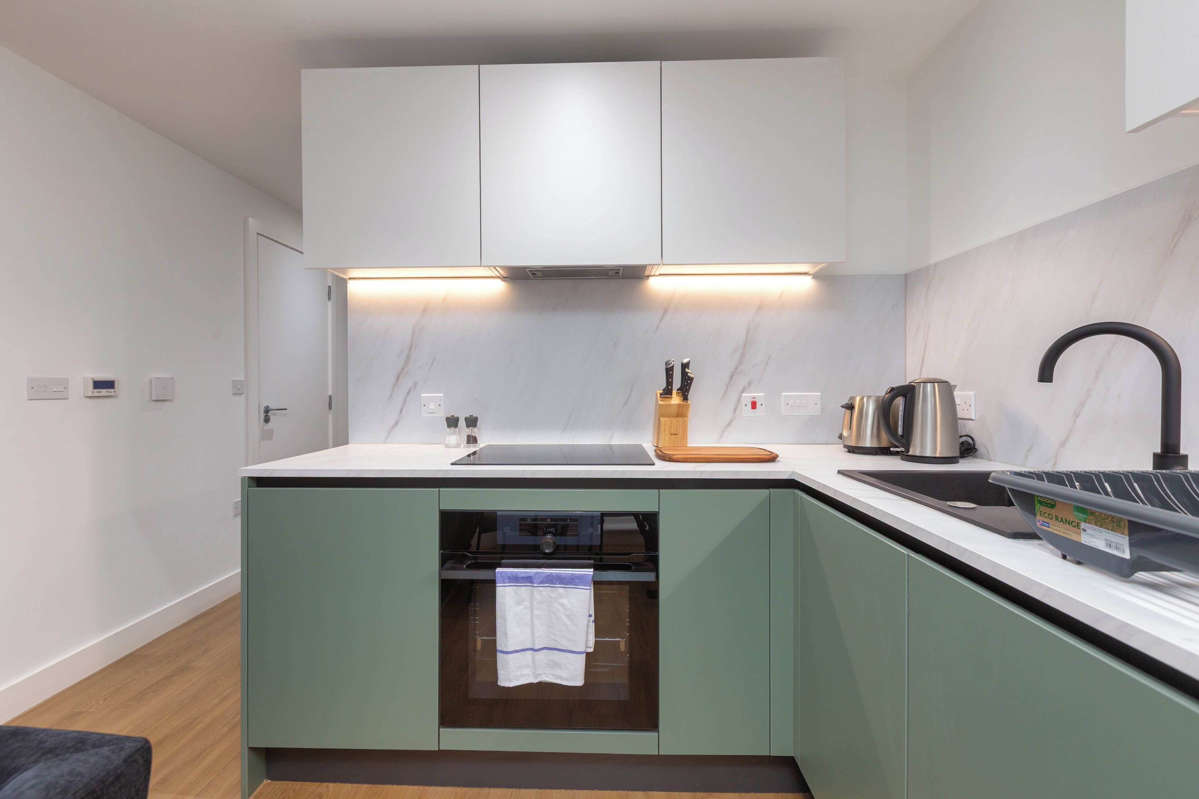 A modern kitchen with a built-in oven, a sink, and a countertop with a kettle and a coffee maker.