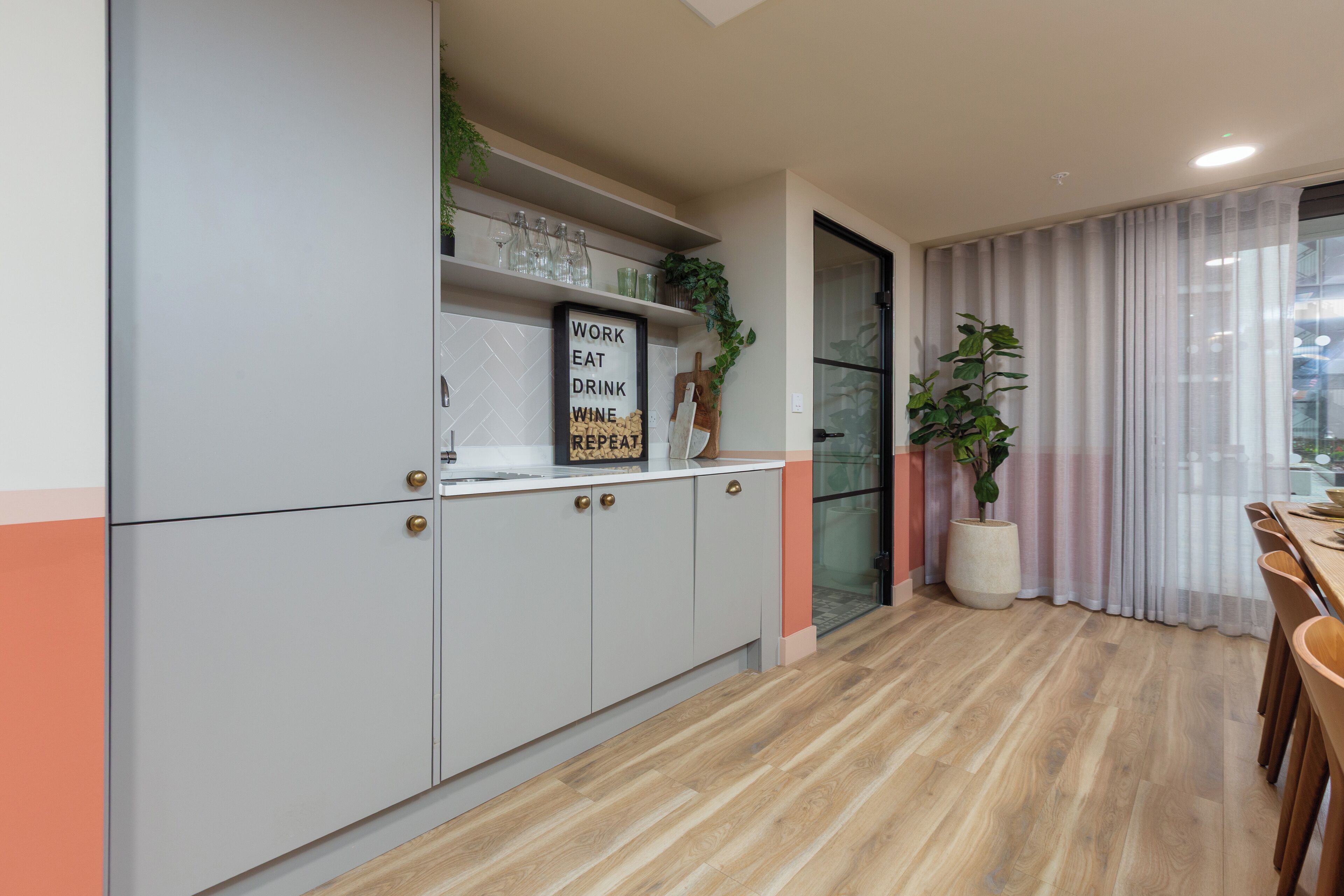 A modern kitchen with grey cabinets, a wooden countertop, and a sign that reads "WORK EAT DRINK".