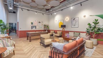 A spacious lounge area with multiple seating options, a pool table, and artwork on the walls.