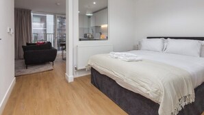 Et moderne hotelværelse med en stor seng, en sort sofa, et spejl og udsigt over byen fra vinduet.