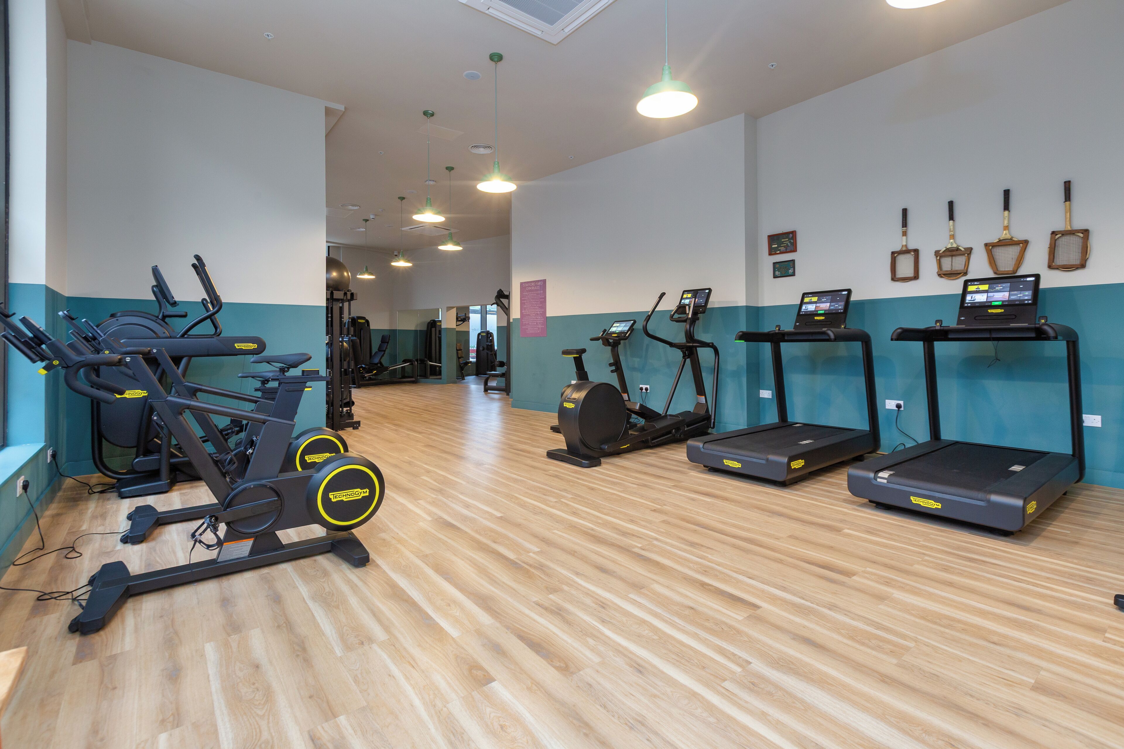 Ein Fitnessraum mit verschiedenen Cardiogeräten, darunter Laufbänder und Crosstrainer, auf Holzboden.