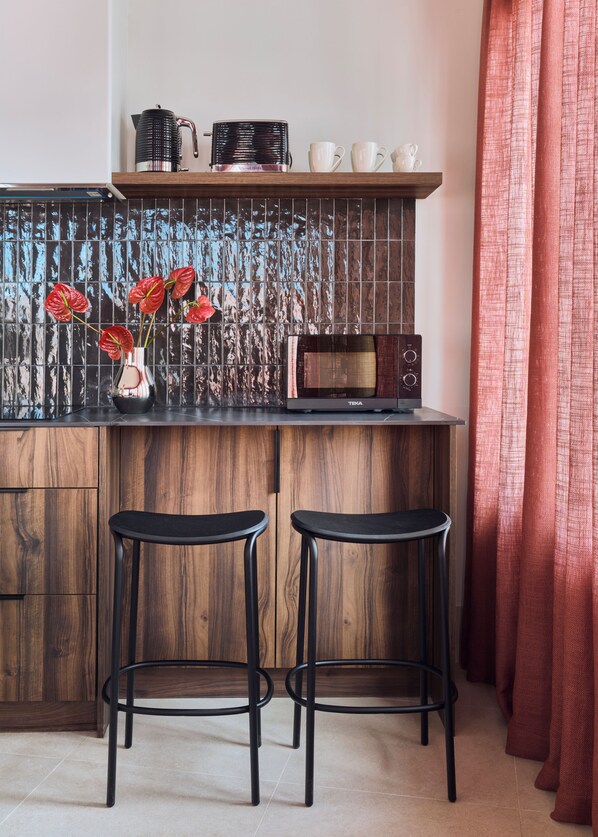 A kitchen with a microwave, two stools, a vase with flowers, and a tiled backsplash.