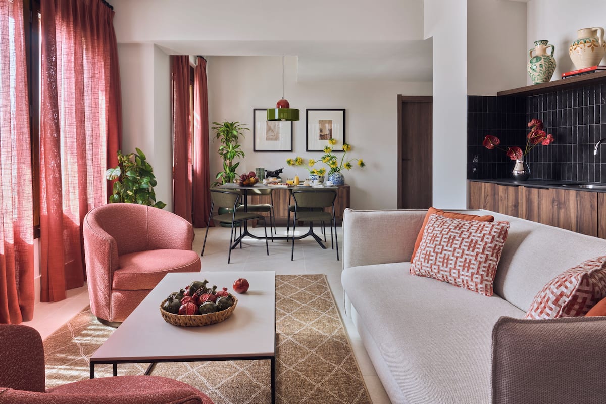 Una sala de estar con sofá, sillón, mesa de comedor, sillas y una zona de cocina con salpicadero negro.