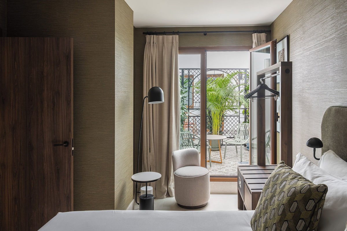 Habitación de hotel con una cama, una mesa redonda, una silla, una lámpara colgante y vistas al exterior.