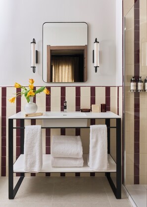 A bathroom with a white sink, a mirror, two wall-mounted lights, a towel rack with towels, and a vase with flowers. - Seda Residences (Granada)