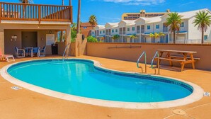 A swimming pool with a wooden deck, lounge chairs, and a building with multiple balconies. - 250 Paces To Beach Pool 1st Floor 2 Bedroom Condo (South Padre Island)