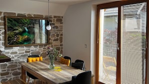 A dining area with a wooden table, benches, and chairs, a stone wall, and a large window with blinds.