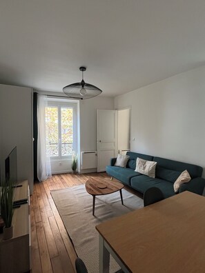 Een moderne woonkamer met een houten vloer, een groene bank, een salontafel en een tv op een dressoir.