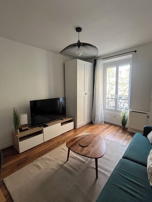 A modern living room with a flat-screen TV, wooden flooring, a green sofa, a coffee table, and a ceiling fan. - Apartment Gare d'Austerlitz - Jardin des plantes (Paris)