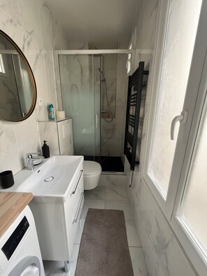 A compact bathroom with a white sink, toilet, and glass-enclosed shower. - Apartment Gare d'Austerlitz - Jardin des plantes (Paris)