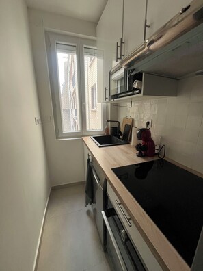 A compact kitchen with a window, a microwave, a stove, and a coffee maker. - Apartment Gare d'Austerlitz - Jardin des plantes (Paris)