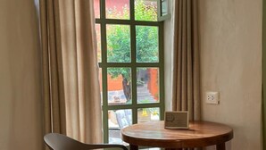 A corner room with a wooden table and a chair, a window with curtains, and a view of greenery outside. -  Casa Terra Cusco (Cusco)
