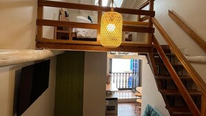 A loft-style room with a wooden staircase, a green door, a sofa, and a hanging light fixture. -  Casa Terra Cusco (Cusco)