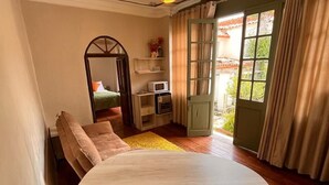 A cozy room with a curved wooden dining table, a comfortable sofa, a small kitchen area, and a large window with curtains. -  Casa Terra Cusco (Cusco)