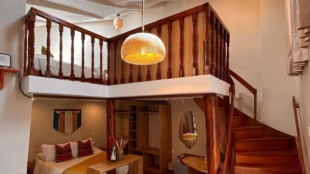 A loft-style bedroom with a wooden staircase, a mezzanine, and a hanging light fixture. -  Casa Terra Cusco (Cusco)