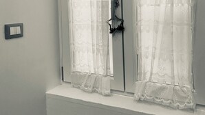 A room with two white-framed windows with lace curtains, a visible door handle, and a light switch on the wall. - Vacation home Queen Matthias (Napoli)
