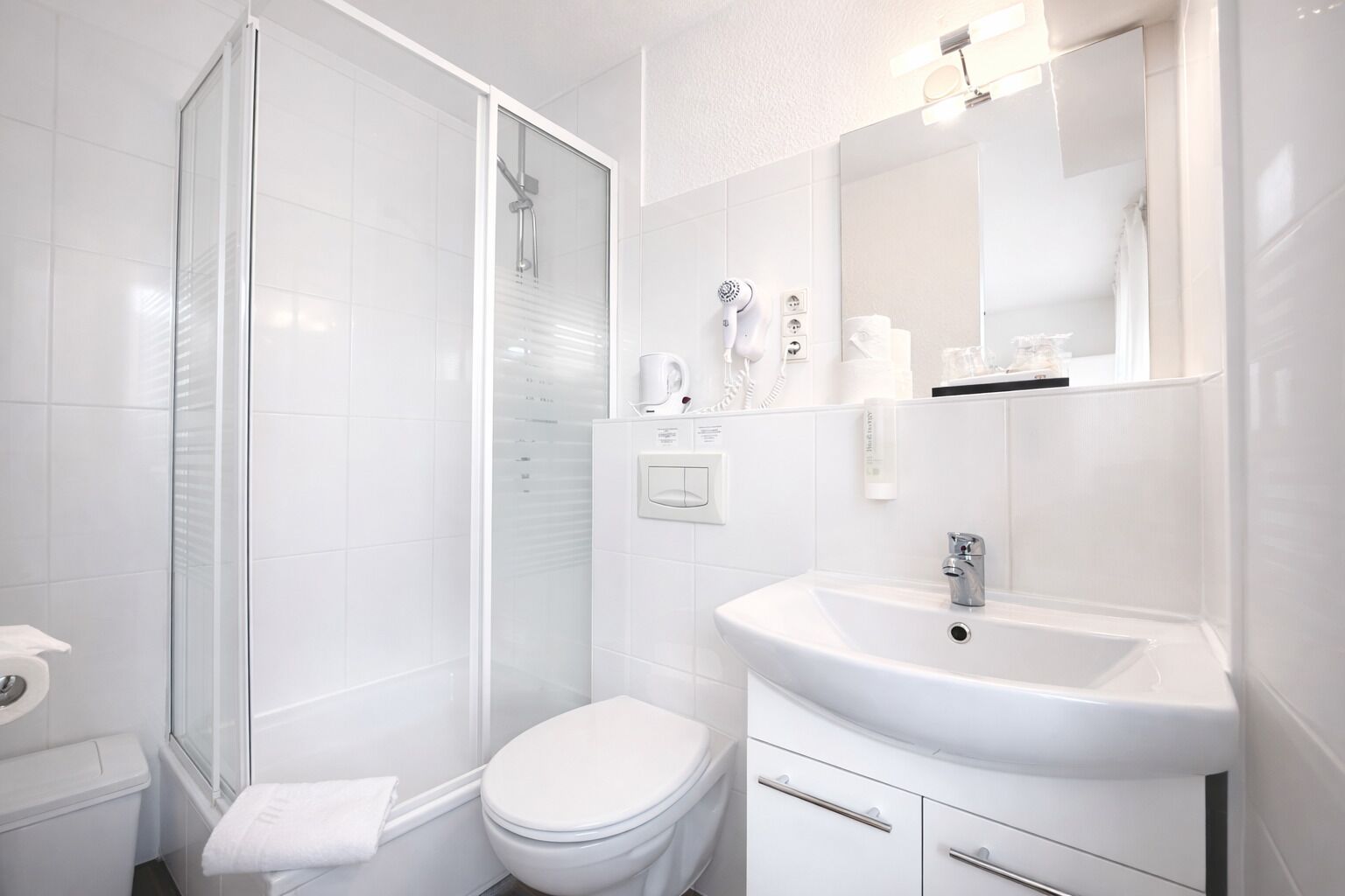 A modern bathroom with a glass-enclosed shower, a white toilet, and a sink with a mirror above it.