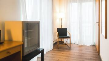 Een hotelkamer met een houten vloer, een televisie op een standaard, een stoel en een lamp.