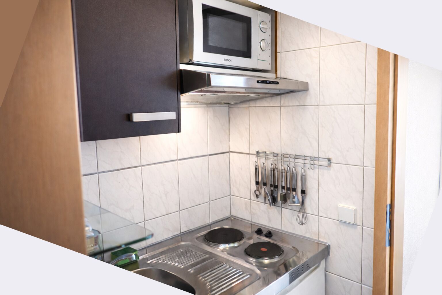 Cocina compacta con un microondas Bosch, una estufa a gas y un organizador de utensilios.