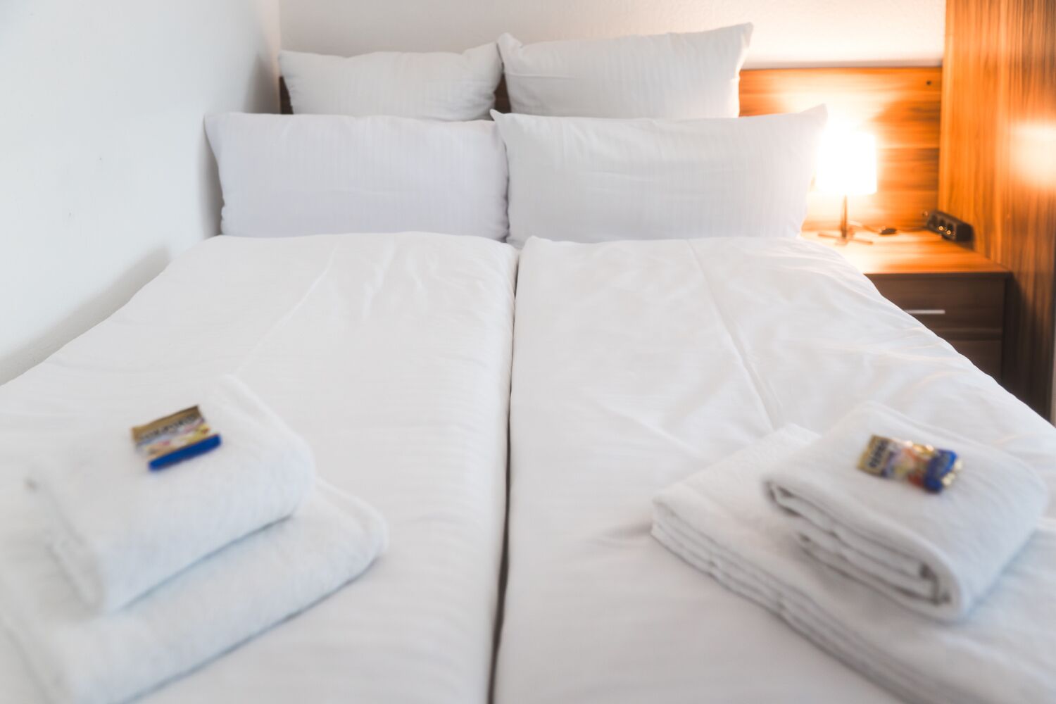 A double bed with white linens and two towels on each side.