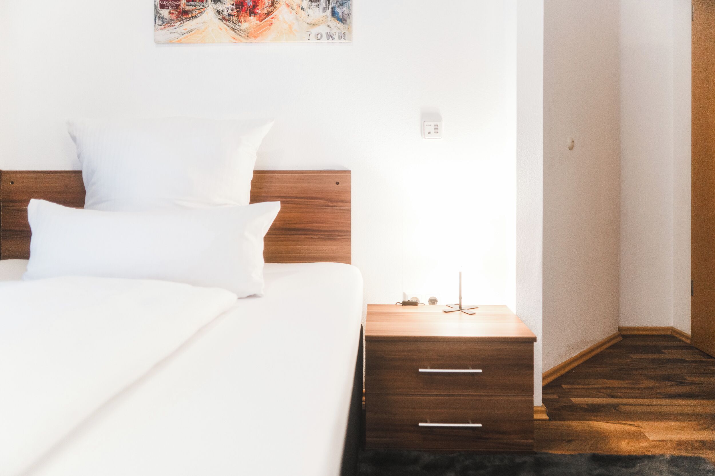 Ein ordentlich bezogenes Bett mit weißen Leinen, ein Holz-Kopfteil und ein kleiner Nachttisch mit Schubladen.
