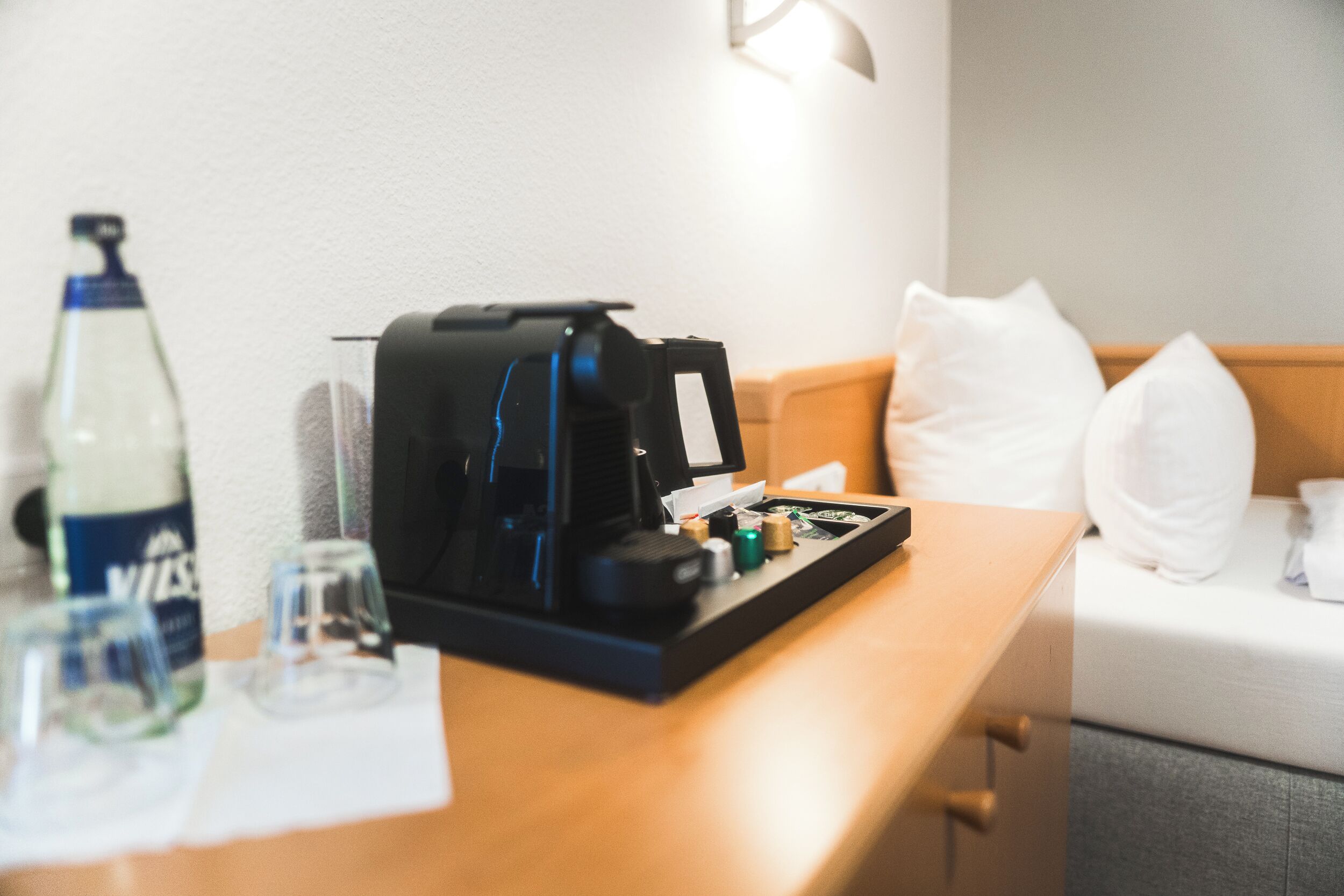Una camera d'albergo con una scrivania in legno, una macchina per il caffè, una bottiglia e dei bicchieri.