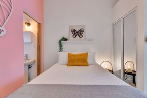 A bedroom with a bed, a bedside table, a wall-mounted shelf with a plant, a wall art piece, and a sliding door. - Love Suite at Miramar, San Juan - 1 Bedroom (San Juan)