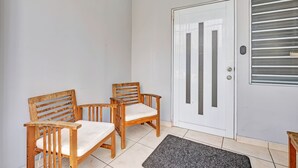 Una habitación con una puerta blanca, dos sillas de madera con cojines y una alfombra pequeña en el suelo.