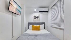 Un dormitorio con cama, televisor de pantalla plana en la pared, aire acondicionado y ventana con persianas.