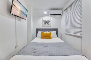 A bedroom with a bed, a flat-screen TV mounted on the wall, an air conditioning unit, and a window with blinds. - Beautiful 2 Bedroom in Miramar! (San Juan)