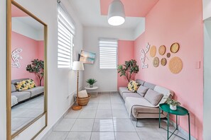 A modern living room with a sofa, a coffee table, and a side table. There is a large mirror, a floor lamp, and a painting on the wall. - Centric, Spacious, Stylish Miramar Unit, Sleeps 4 (San Juan)