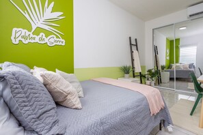 Ein Schlafzimmer mit einem Bett, einer grünen Wand mit Palmenblatt-Dekoration, einer Schiebetür aus Glas und einem kleinen Tisch mit Stühlen.