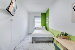 A hotel room with a bed, a desk, a plant, and a green accent wall. - Bright, Centric and Cozy Studio In The Heart of Miramar (San Juan)
