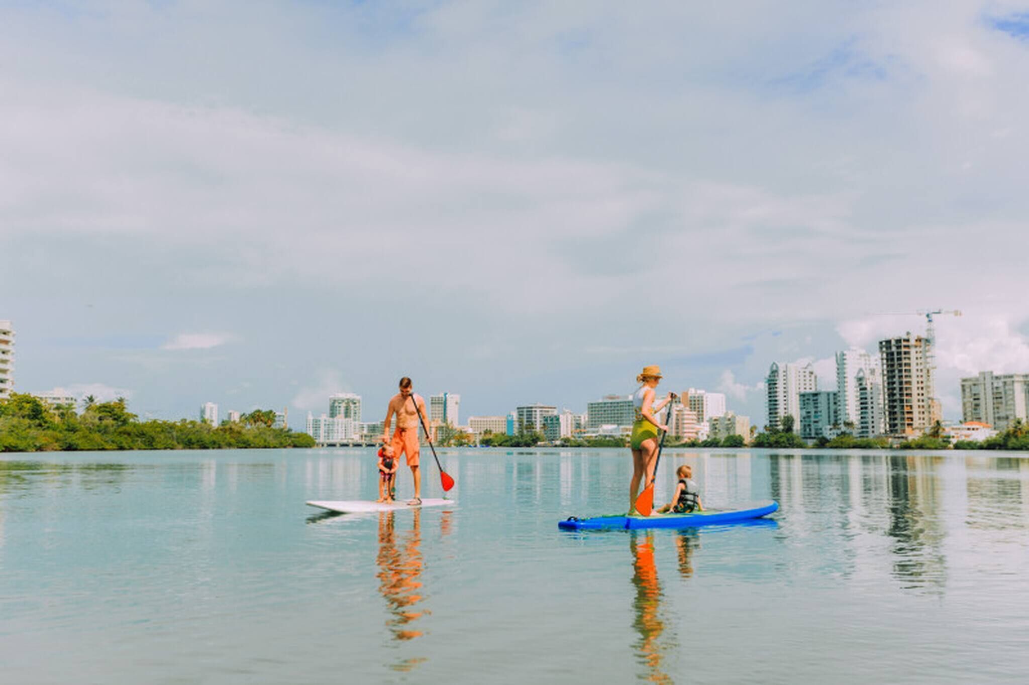Vista al agua con tablas de remo y un barco pequeño, edificios al fondo y agua tranquila.