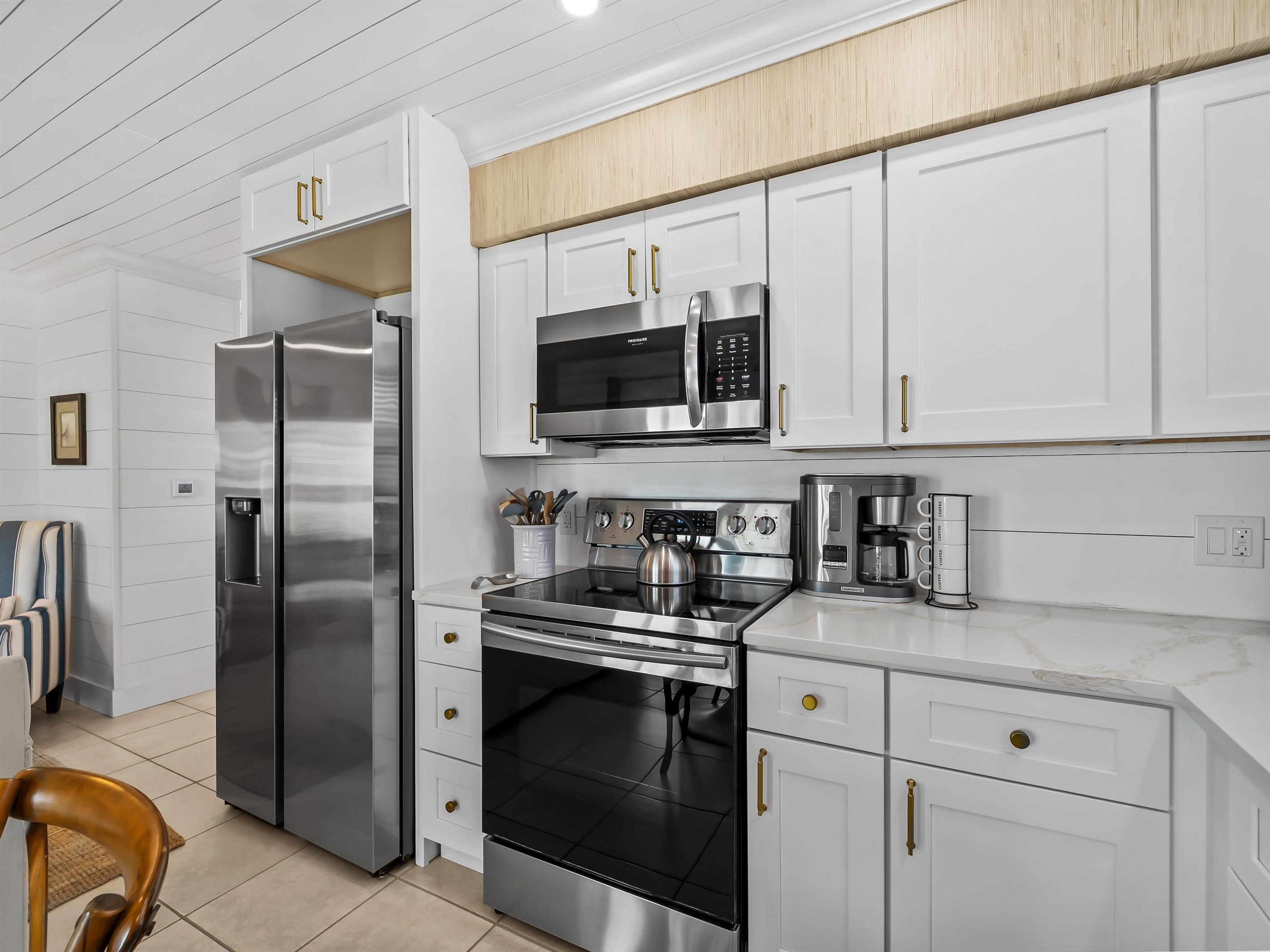 A modern kitchen with stainless steel appliances, white cabinetry, and a wooden ceiling.