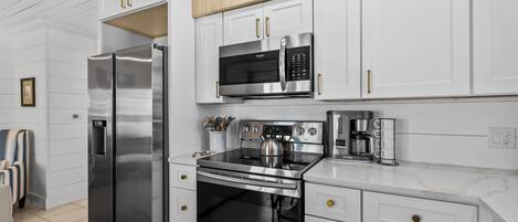 A modern kitchen with stainless steel appliances, white cabinetry, and a wooden ceiling.