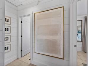 Un couloir avec une grande peinture abstraite au mur, une porte et des œuvres d’art encadrées sur le côté gauche.