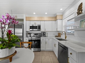 Une cuisine moderne avec des meubles blancs, des appareils en acier inoxydable et un îlot central agrémenté d’une plante en pot.