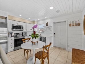 A modern kitchen with white cabinetry, stainless steel appliances, and a dining area with a round table and wooden chairs. - Seahorse Cottage 1 | Coastal Hideaway with Private Beach (Englewood)