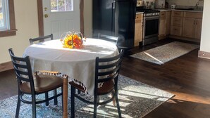 Un comedor con una mesa dispuesta para cuatro personas, un refrigerador negro, un microondas y una estufa en la cocina contigua.